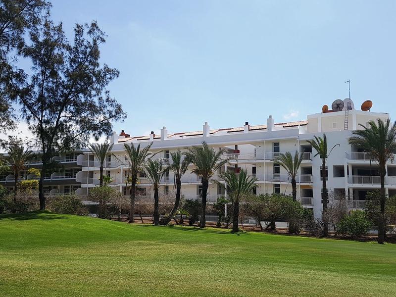 Biały budynek hotelu z palmami i zielonymi trawnikami pod czystym niebem.