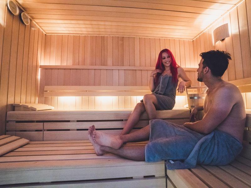 Dwie osoby relaksują się w drewnianej saunie z ciepłym oświetleniem.