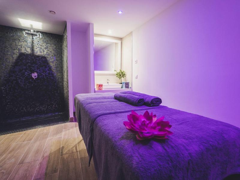 Relaksujący pokój do masażu z fioletowo oświetlonym łóżkiem i kwiatem.