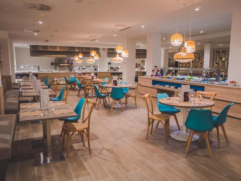 Nowoczesna restauracja hotelowa z miejscami do siedzenia, drewnianymi stołami i niebieskimi krzesłami w ciepłym oświetleniu.