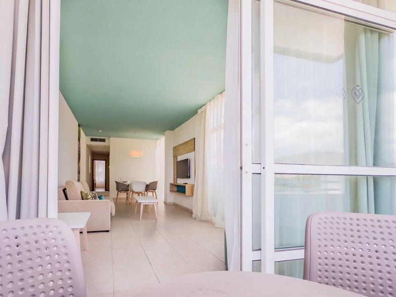 Nowoczesny, jasny pokój hotelowy z miejscami do siedzenia i dużym balkonem ze szklaną balustradą.