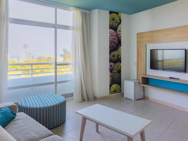 Nowoczesny pokój hotelowy z balkonem, dużym oknem i jasnym umeblowaniem.