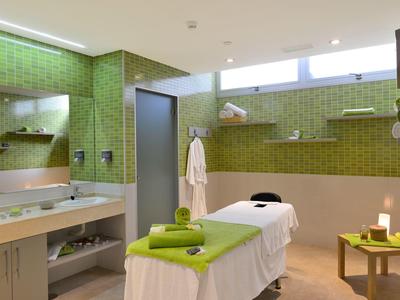 Bright massage room with green wall tiles, massage table, and towels for relaxation.