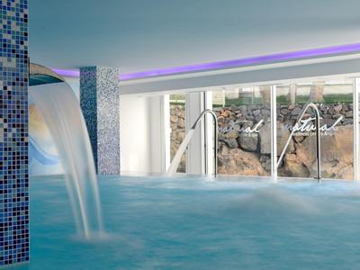 Indoor pool with waterfall, large windows, and ambient lighting.