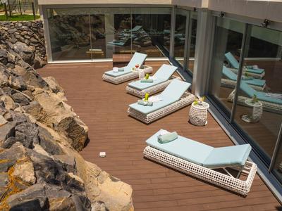 Comfortable lounge chairs with towels on wooden terrace beside hotel windows and rocks.