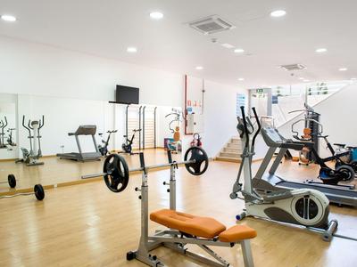 Helle Fitnessraum mit Hantelbänken, Cardio-Geräten und großen Spiegeln an der Wand.