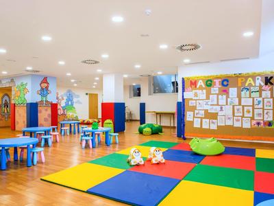 Colorful play area with tables, chairs, and carpet for children in a bright room.