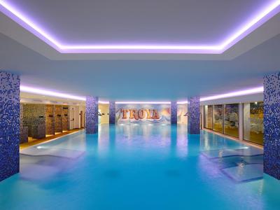 Piscina coperta moderna con piastrelle blu e illuminazione LED atmosferica su soffitto e colonne.