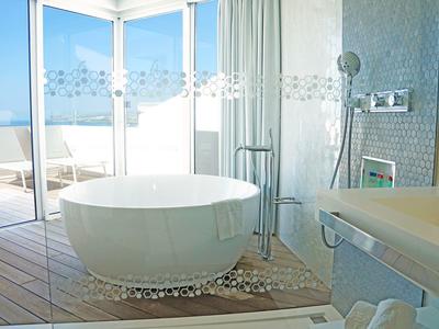 Bright bathroom with freestanding bathtub and large windows overlooking the sea.