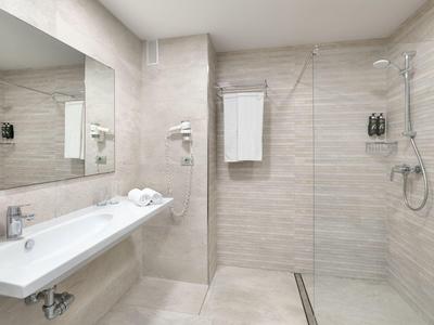Modern hotel bathroom with large walk-in shower, sink, and illuminated mirror.