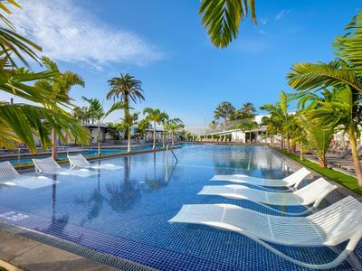 Moderner Poolbereich mit Liegestühlen im Wasser und Palmen an einem sonnigen Tag