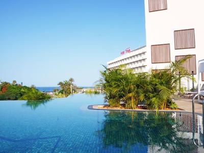 Moderner Hotelpool mit Liegestühlen und Palmen unter einem klaren blauen Himmel.
