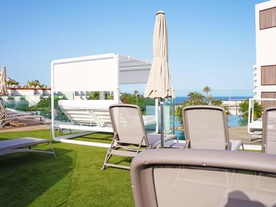 Hotel terrace with lounge chairs, parasol, and sea view under a clear sky.