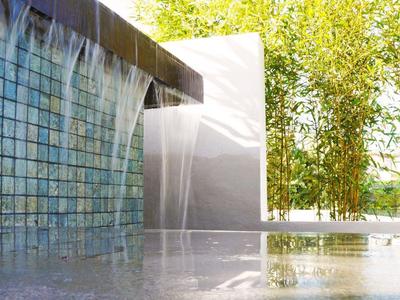Modern waterfall with blue tiles and green trees in the background in daylight.