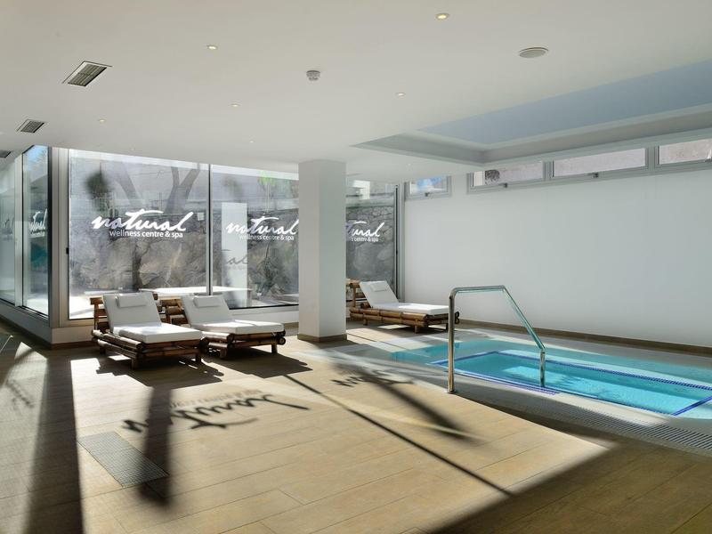 Bright indoor pool with several lounge chairs by the window and a calm atmosphere.