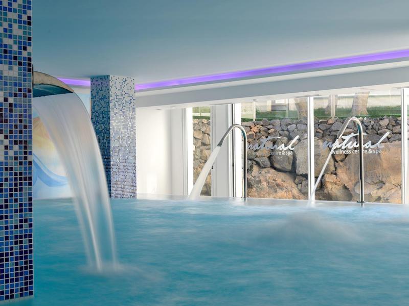 Indoor pool with waterfall, large windows, and ambient lighting.