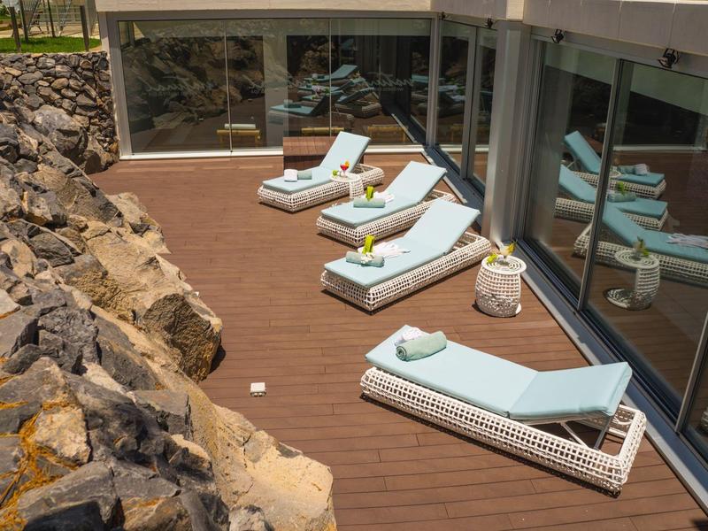 Comfortable lounge chairs with towels on wooden terrace beside hotel windows and rocks.