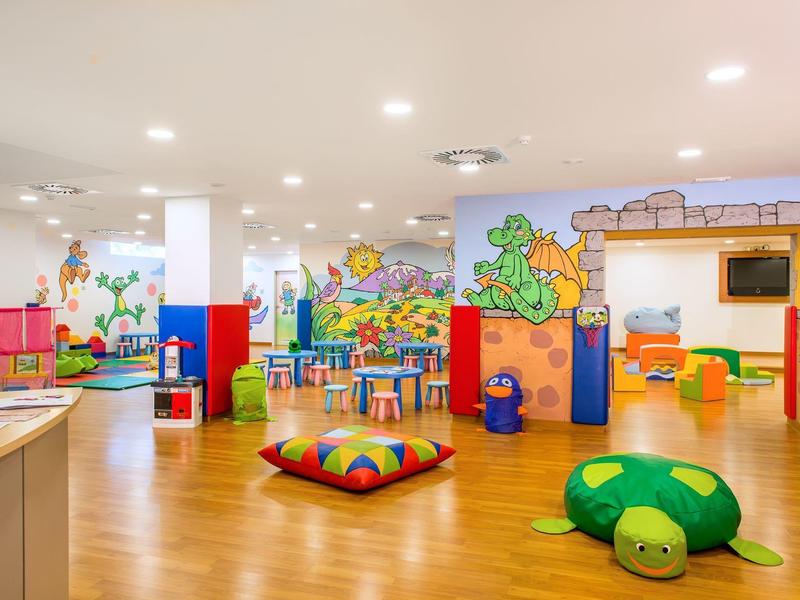 Colorful children's playroom with soft cushions, tables, chairs, and wall murals.