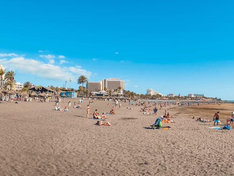 Wide sandy beach with people and city in the background under clear sky.