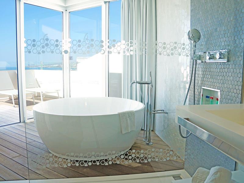 Bright bathroom with freestanding bathtub and large windows overlooking the sea.
