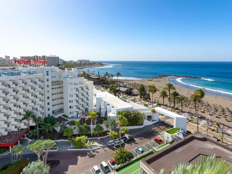 View of a large hotel by the sandy beach overlooking the blue sea under a clear sky.