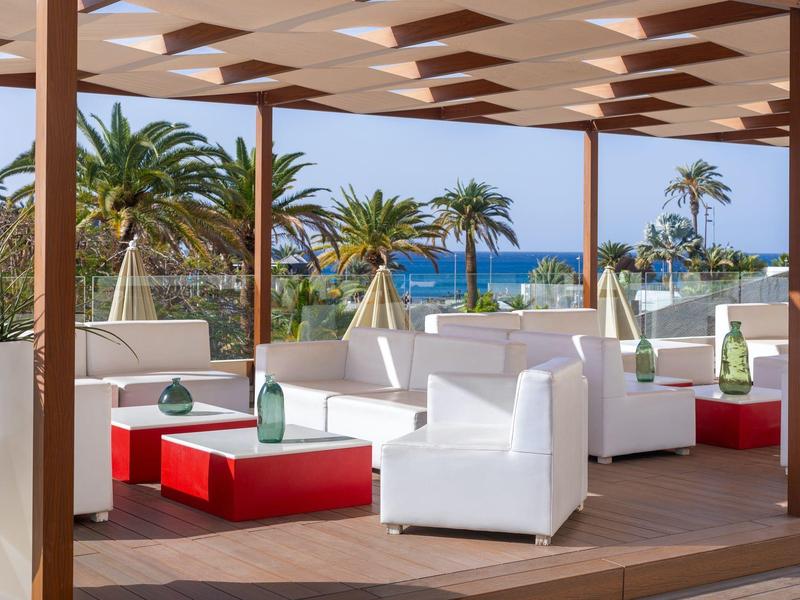 Modern lounge with white furniture overlooking palm trees and the sea.