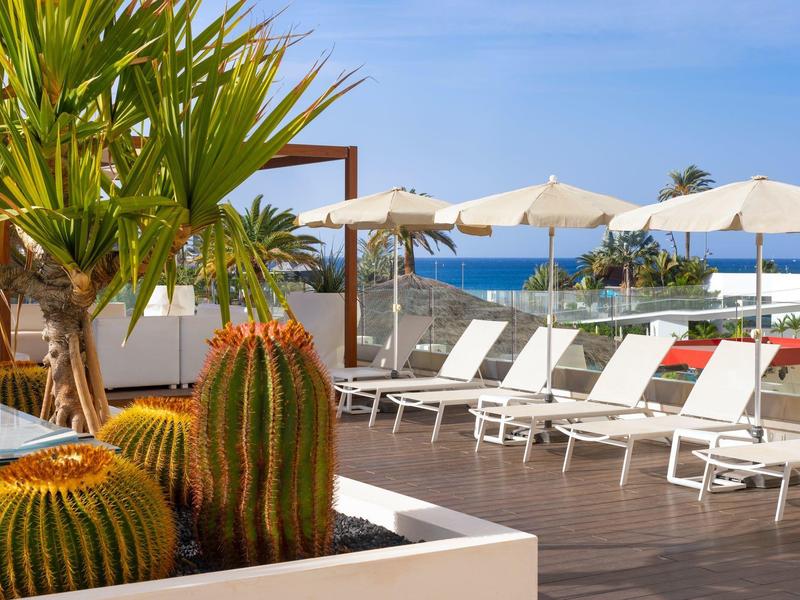 Pool terrace with sun loungers, umbrellas, and cacti overlooking the sea.