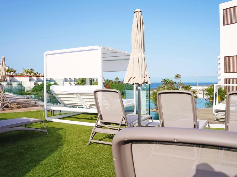 Hotel terrace with lounge chairs, parasol, and sea view under a clear sky.