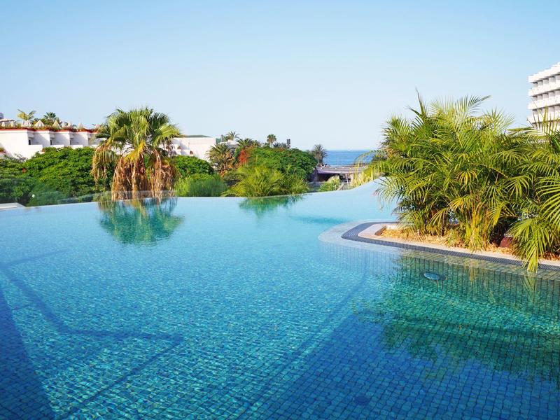 A serene hotel pool with clear water, surrounded by plants and direct sea view.