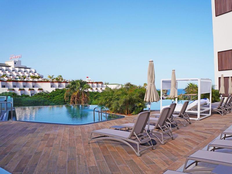 Inviting outdoor pool with sun loungers and umbrellas on a wooden deck under clear sky.