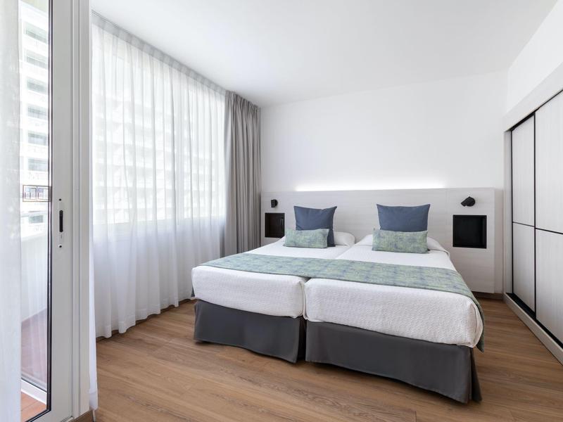 Bright hotel room with two single beds, large window, and modern wooden flooring.