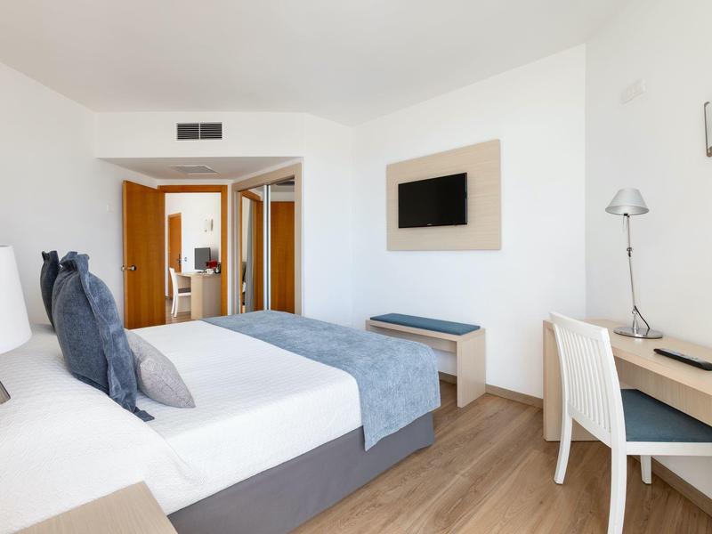 Modern hotel room with double bed, desk, and flat-screen TV mounted on the wall.