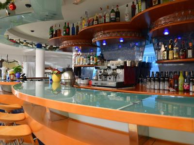 Moderne Bar mit hellen Holzstühlen, glatter Glasfläche und beleuchteten Regalen mit Flaschen.