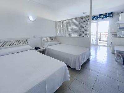 Hell eingerichtetes Schlafzimmer mit zwei weißen Betten und Zugang zu einem Balkon.