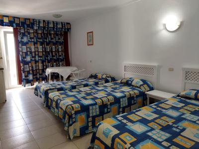 Zimmer mit zwei Einzelbetten, farbenfrohen Bettdecken, weißen Wänden und Fliesenboden.