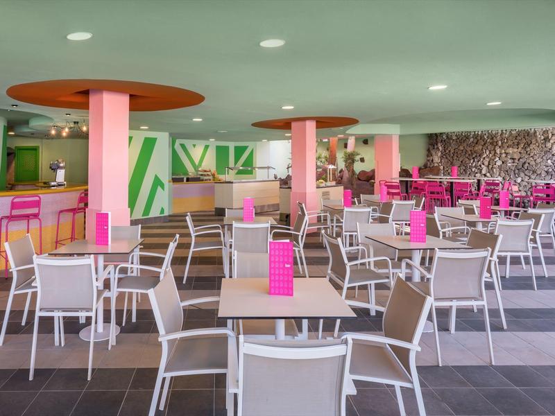 Nowoczesna restauracja z białymi krzesłami, drewnianymi stołami i różowymi akcentami.