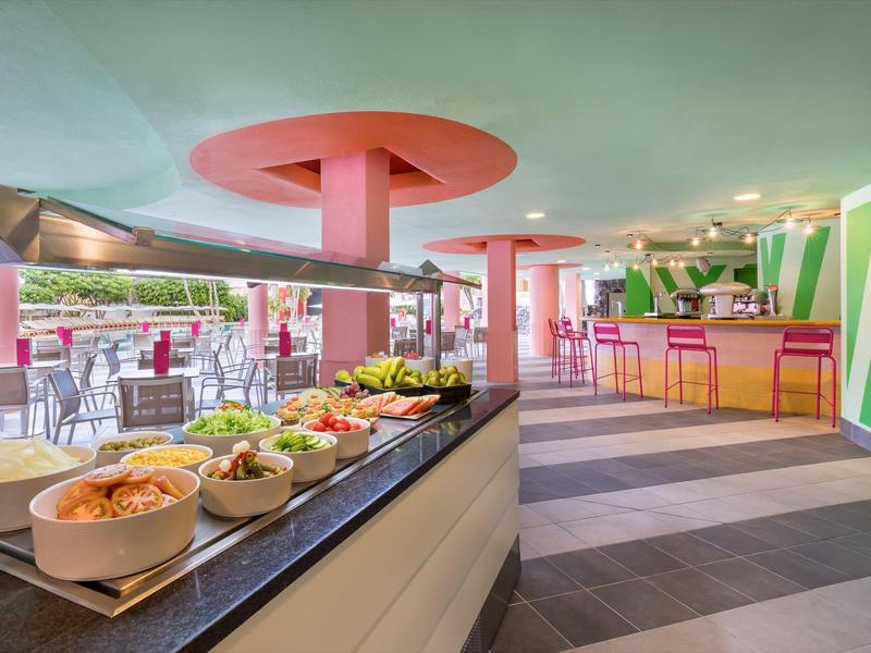 Kolorowy bufet śniadaniowy z widokiem na słoneczny taras i nowoczesny bar.