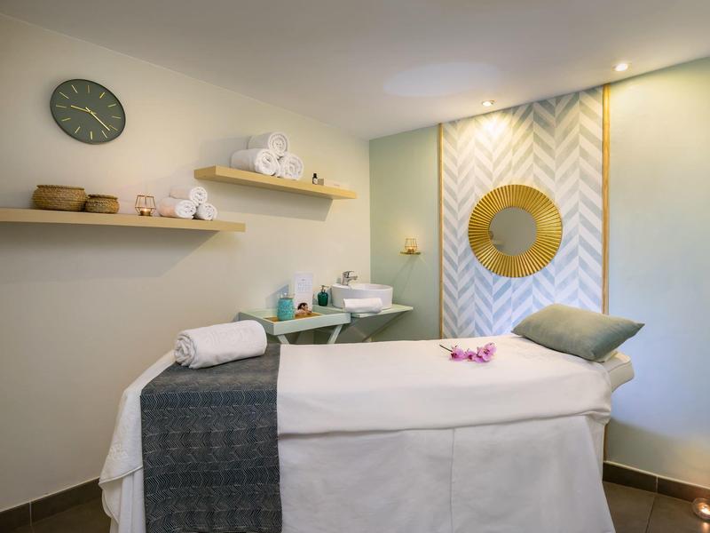 Strefa masażu z łóżkiem, ręcznikami i delikatną, jasną dekoracją.