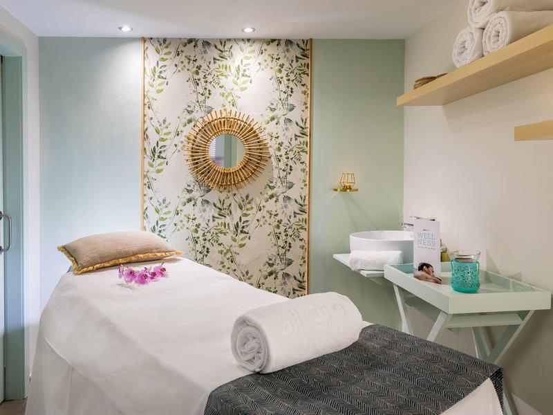 Spokojny pokój zabiegowy z łóżkiem do masażu i kwiatową dekoracją.