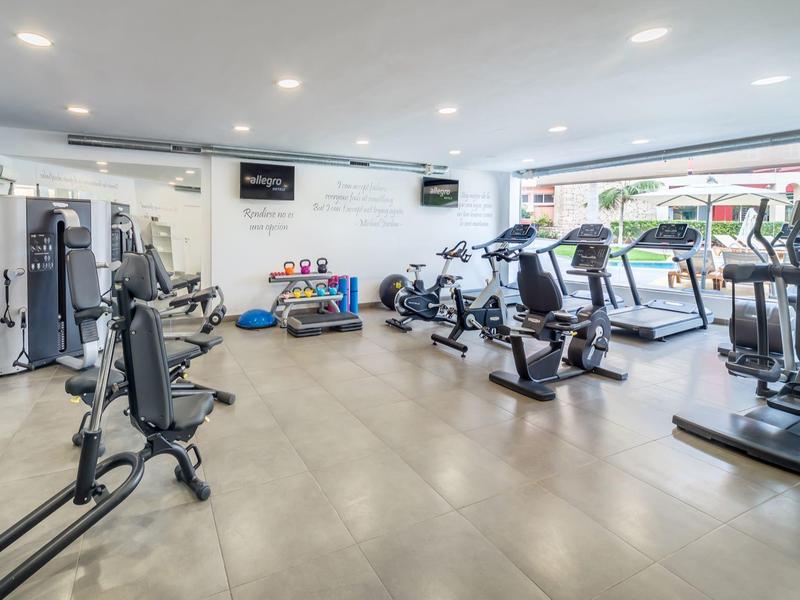 Przestronna siłownia z nowoczesnym sprzętem i dużymi oknami z widokiem na zewnątrz.