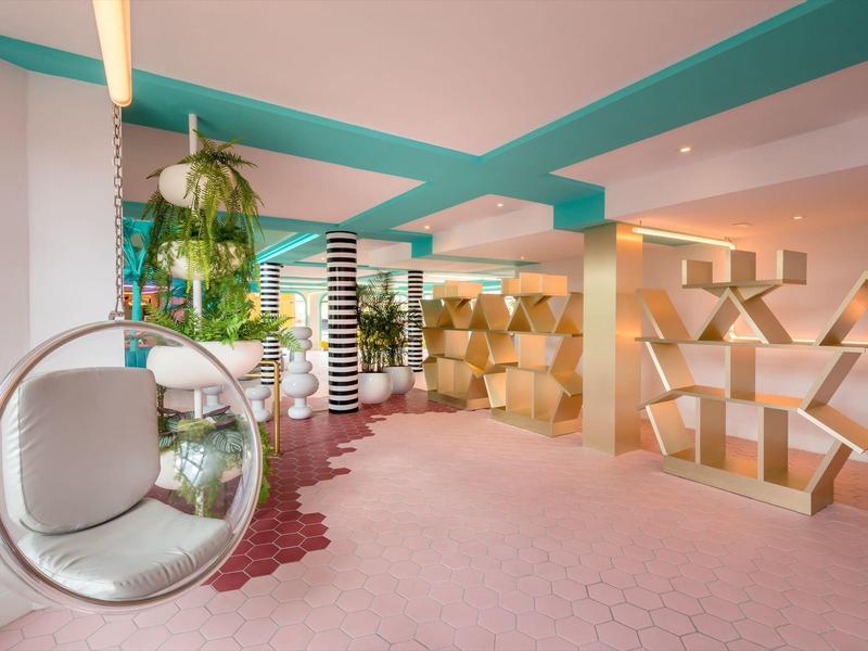 Nowoczesne wnętrze hotelu z wiszącym fotelem, roślinami i geometrycznymi dekoracjami.