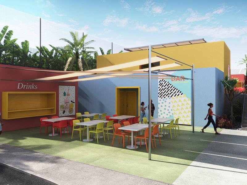 Kolorowy taras z stołami i krzesłami przed budynkiem o wielobarwnych ścianach pod niebieskim niebem.