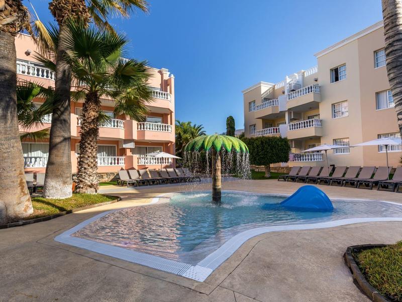 Basen na zewnątrz z leżakami, palmami i budynkami mieszkalnymi w tle.