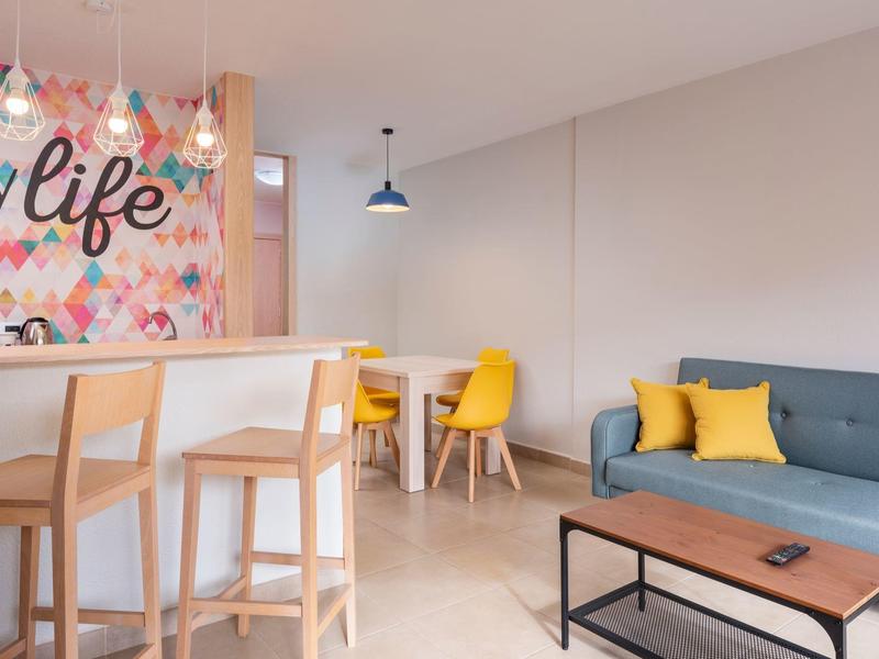 Nowoczesny salon z szarą sofą, żółtymi krzesłami i kolorową dekoracją ścienną.