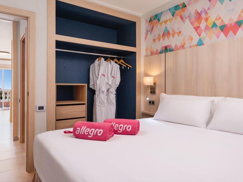 Nowoczesny pokój hotelowy z łóżkiem podwójnym, szlafrokami i kolorową otwartą szafą.