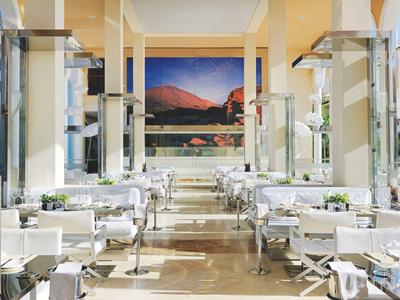 Elegante hotelrestaurant met witte zitplaatsen en een groot landschapsschilderij op de achterwand.