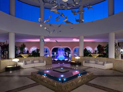 Elegante Hotel-Lounge mit runder Glasdecke, Sofas und zentralem beleuchtetem Wasserbecken.