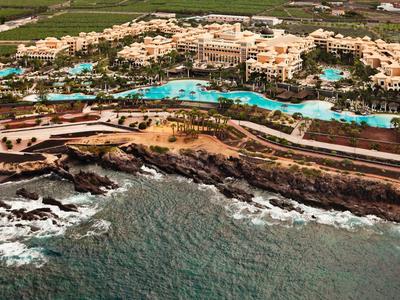 Kustresort met meerdere zwembaden, tuinen en gebouwen aan een rotsachtige oceaankust.