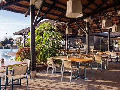 Offener Hotelrestaurantbereich mit Gartenmöbeln neben dem Pool unter Holzpergola.