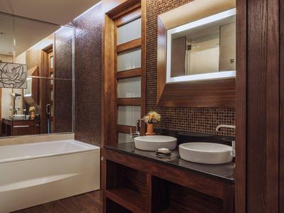 Moderne badkamer met dubbele wastafels, houten kasten en een ligbad naast een spiegelwand.